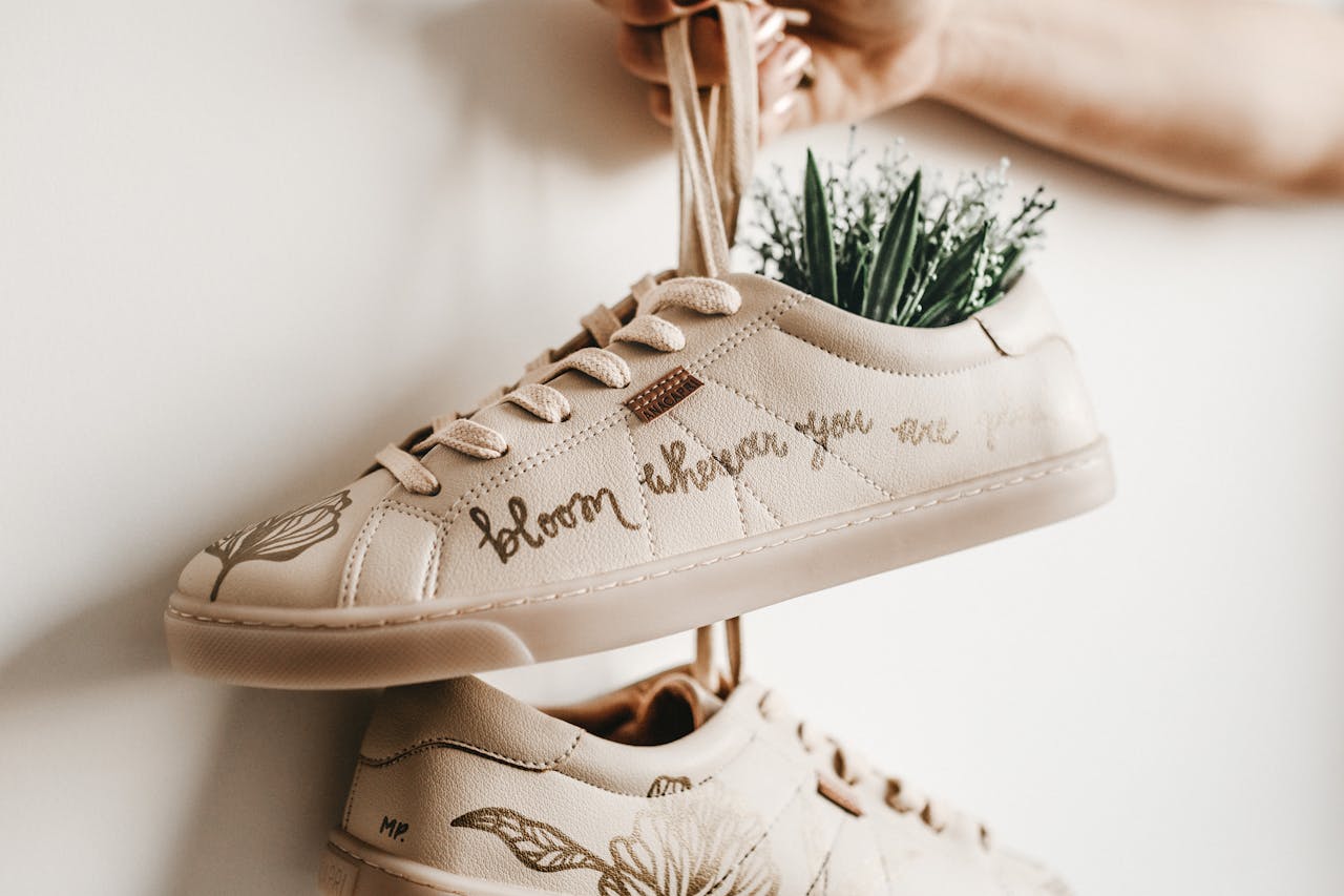 Close-up of beige sneakers with plant design and 'bloom where you are planted' script.